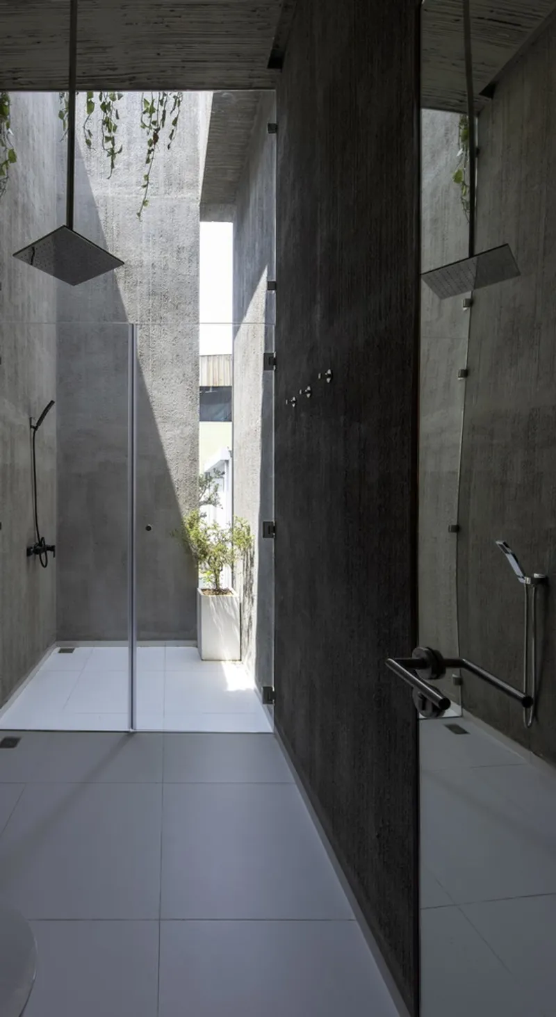 Narrow bathroom corridor with dark timber wall divider and glazed shower opening to a planted courtyard