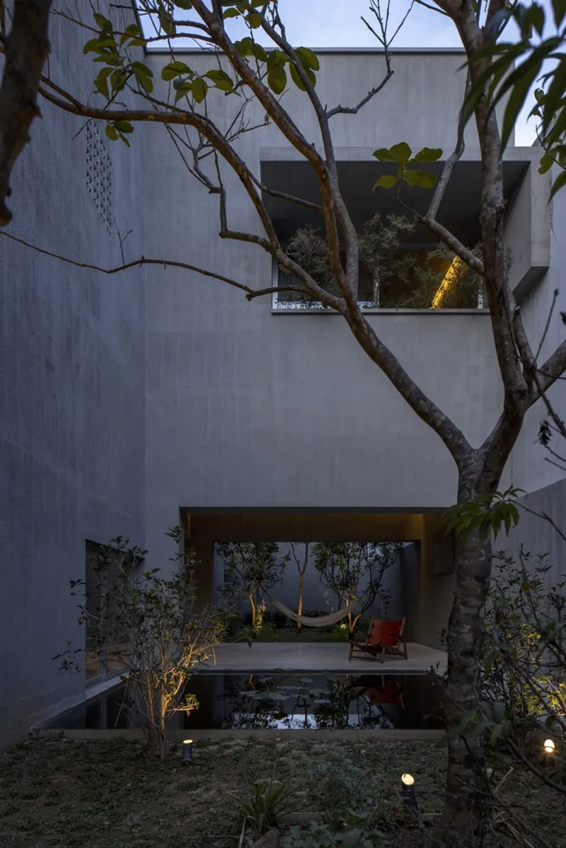 Concrete facade with cantilevered terrace framed by bare branches at dusk
