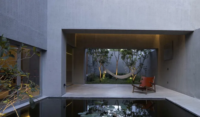 Covered terrace overlooking a reflecting pool with hammock strung between trees in the courtyard beyond