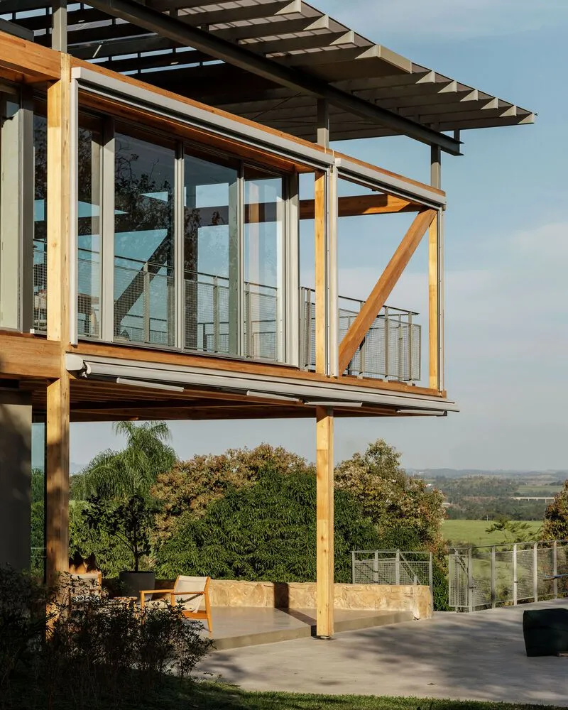 Upper-level glass-enclosed volume with timber bracing and pergola overhang at golden hour