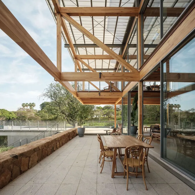 Covered terrace with timber pergola, dining table and stone planters facing the open fields