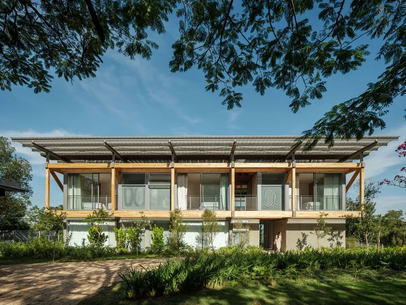 Front facade showing glazed upper level with exposed timber structure and row of young trees below