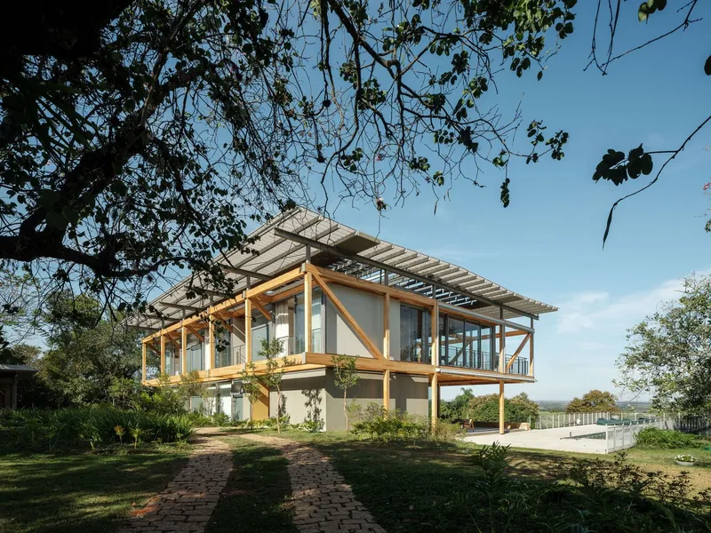 Corner view of the cantilevered timber frame with diagonal bracing framed by overhanging tree branches