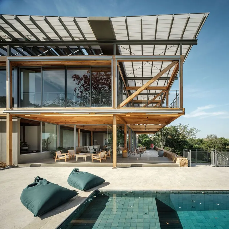 Double-height terrace with swimming pool and outdoor seating beneath stacked timber frames and solar canopy