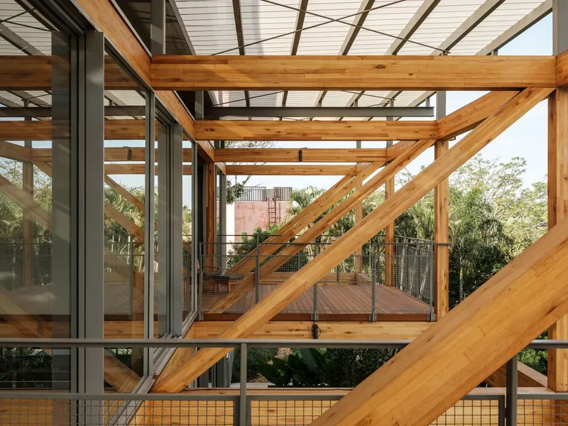Exposed timber framing with diagonal bracing and elevated walkway connecting interior volumes