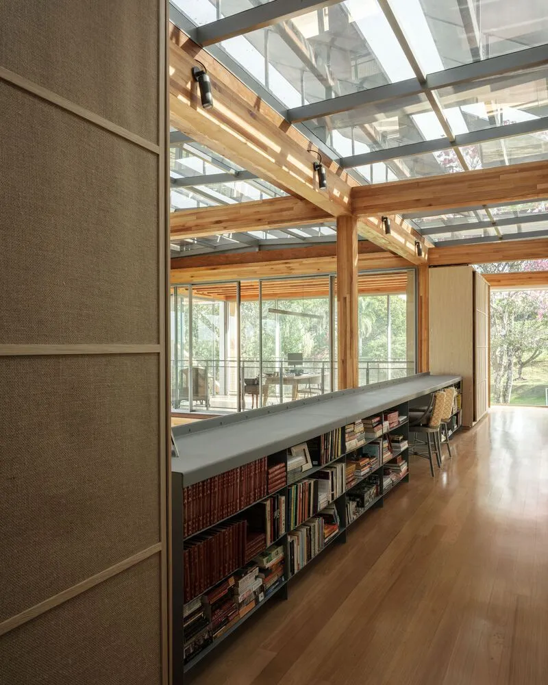 Low bookshelf dividing the hallway beneath timber joists and glazed roof panels with garden views beyond