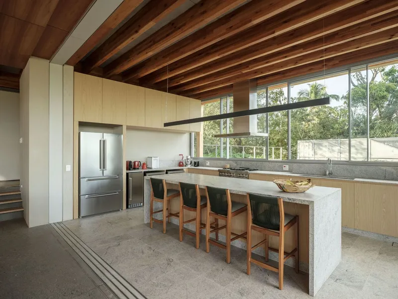 Kitchen with pale wood cabinetry, marble island and clerestory windows facing trees