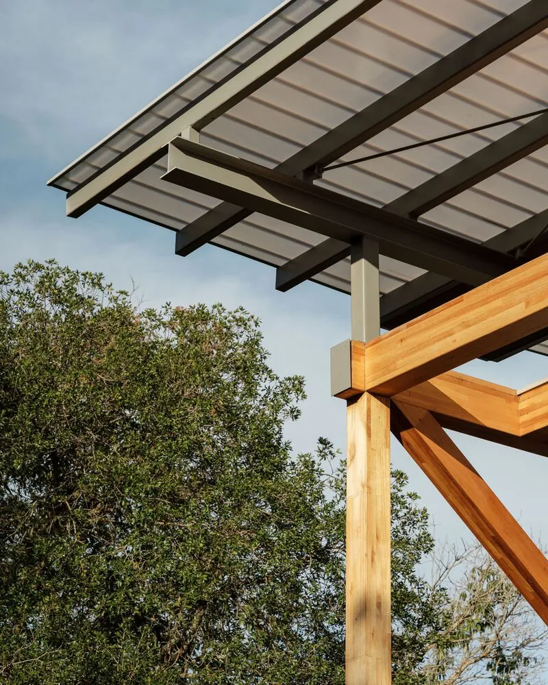 Detail of cantilevered roof with translucent panels supported by steel and timber beams against sky