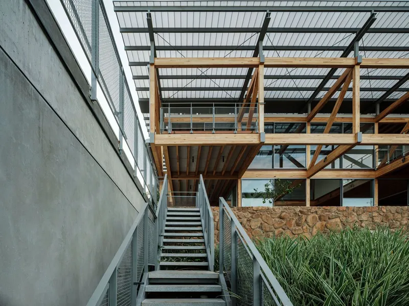 Exterior staircase ascending between concrete retaining wall and exposed timber frame structure with planted bed