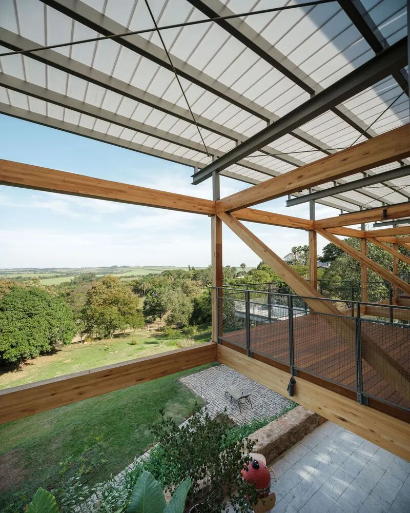 Planted courtyard beneath glazed roof with timber beams and steel cross-bracing overlooking open landscape