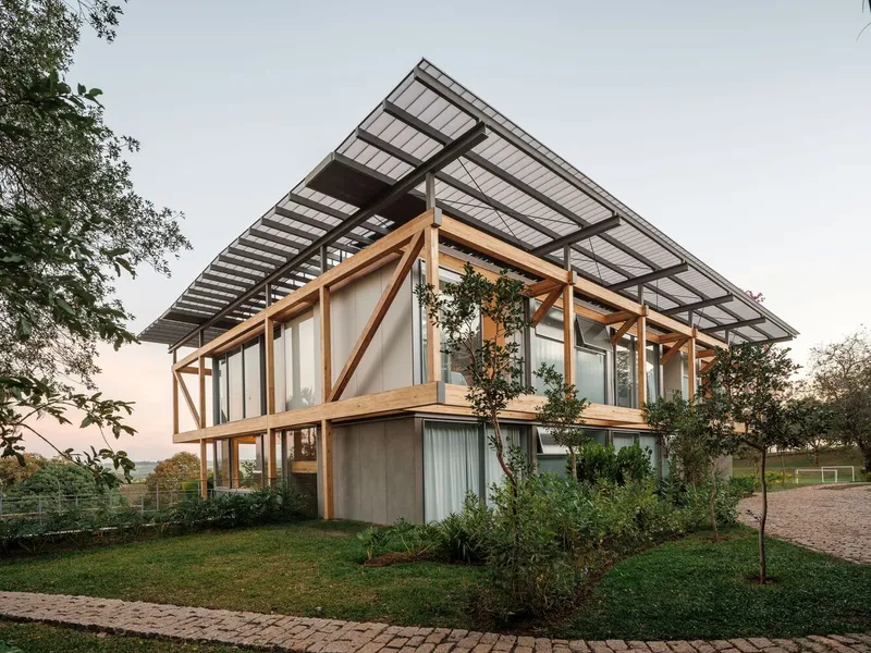 Timber-framed facade with exposed diagonal bracing and solar panel canopy at dusk surrounded by lawn and trees