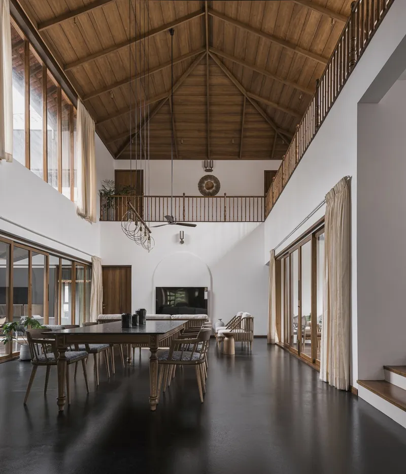 Double-height dining space with exposed timber gable ceiling and arched fireplace opening in white plaster