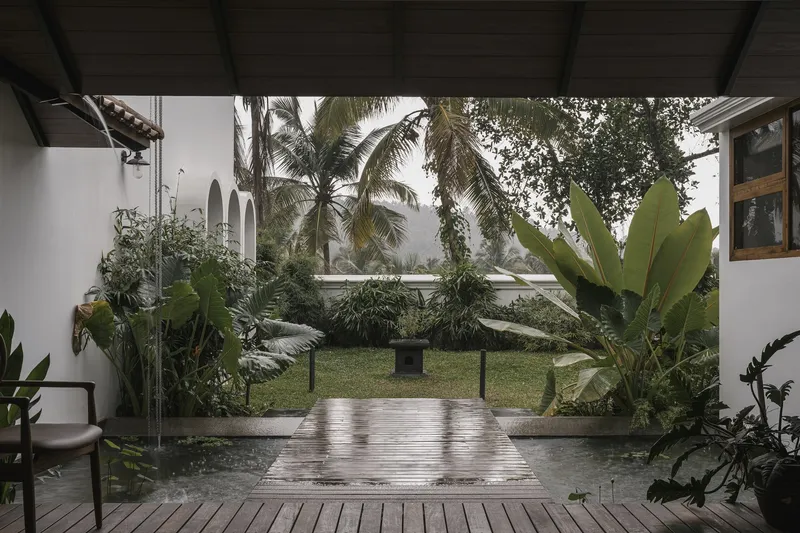 Covered terrace overlooking a lawn courtyard framed by coconut palms and tropical vegetation after rain