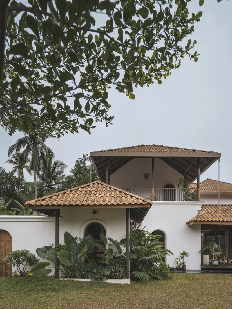 Garden view of white stucco volumes with arched openings and terracotta tile roofs beneath palm trees
