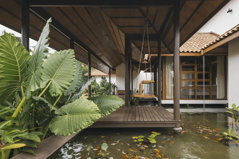 Covered deck platform with hanging swing overlooking a koi pond with lily pads and elephant ear plants