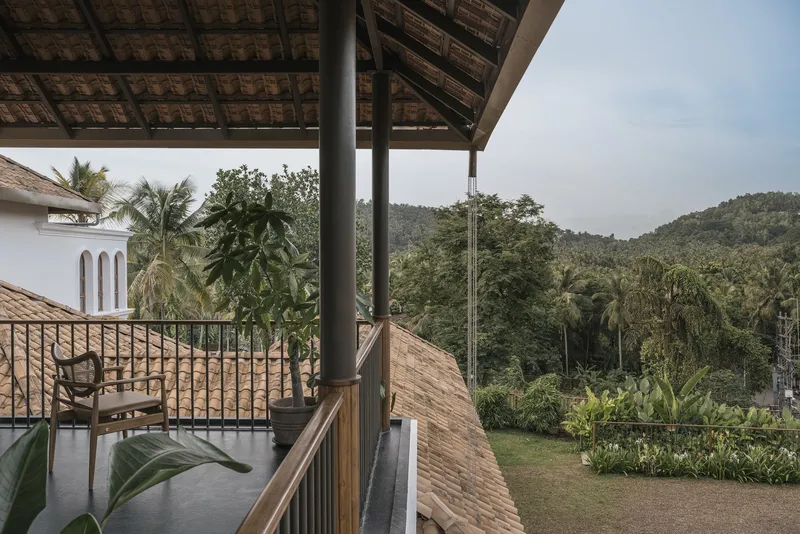 Upper-level covered balcony with clay tile roof overlooking forested hills under overcast sky