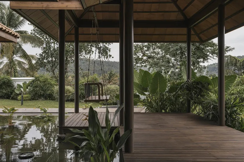Open pavilion with timber decking and a hanging swing seat beside a reflecting pool and banana plants