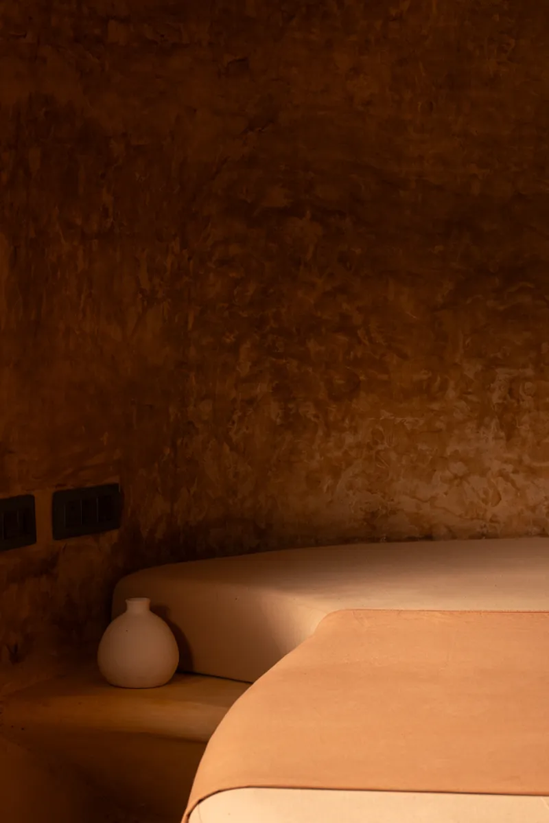 Bedroom: round earthen bed with cushion, vaulted ceiling, small window, pendant light, monastic calm