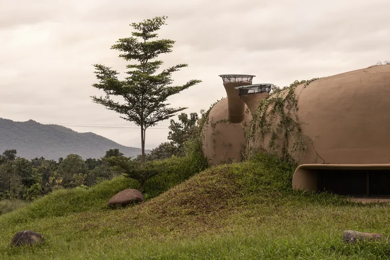 Ventilation chimney and wall: funnel-shaped earth vent emerging from grass-covered roof, vine on wall, trees, mountains