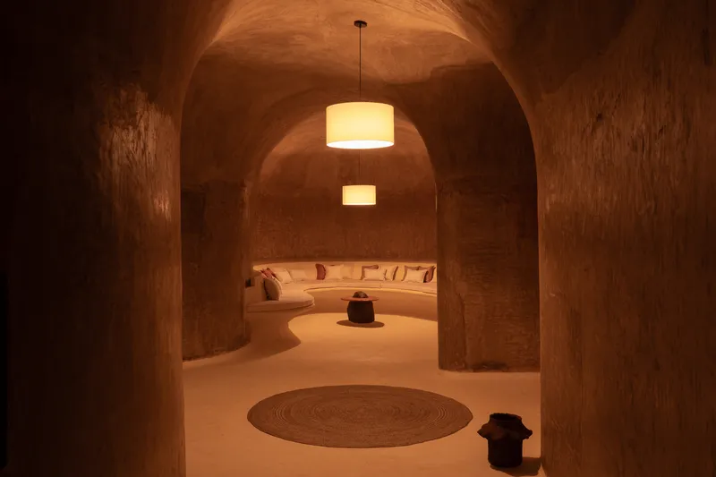 Living corridor at night: arched vaults receding in perspective, curved sofa at the end, jute rugs, warm light
