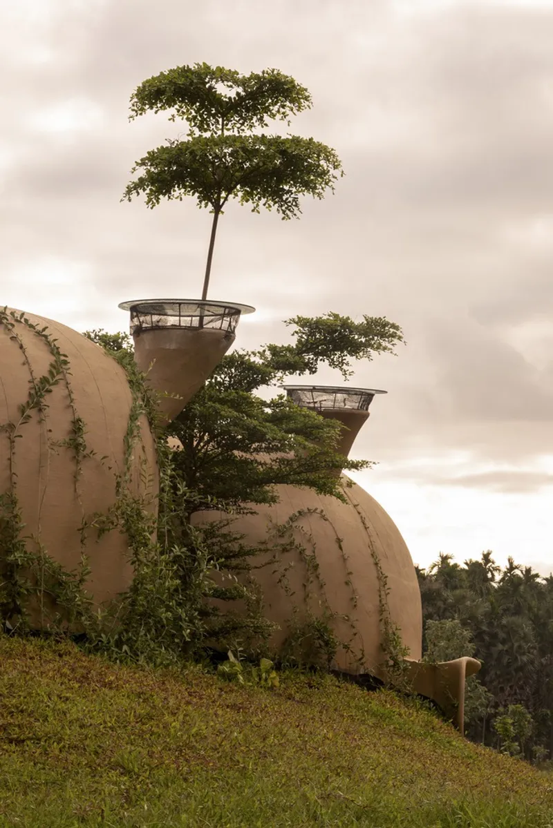 Ventilation towers: two funnel-shaped earth chimneys rising above the grass roof, vines, trees, overcast sky