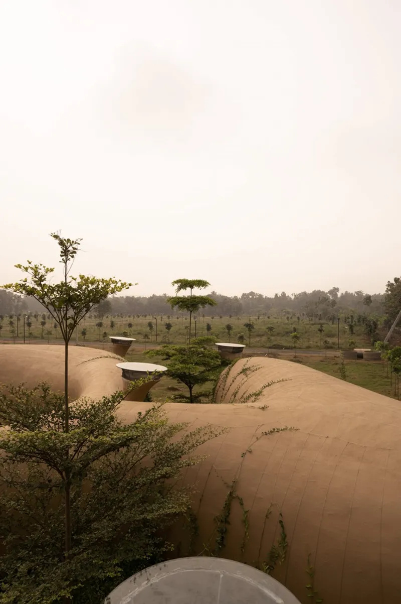 Rooftop perspective: earth walls curving between lobes, ventilation funnels, landscape mounds, misty fields beyond