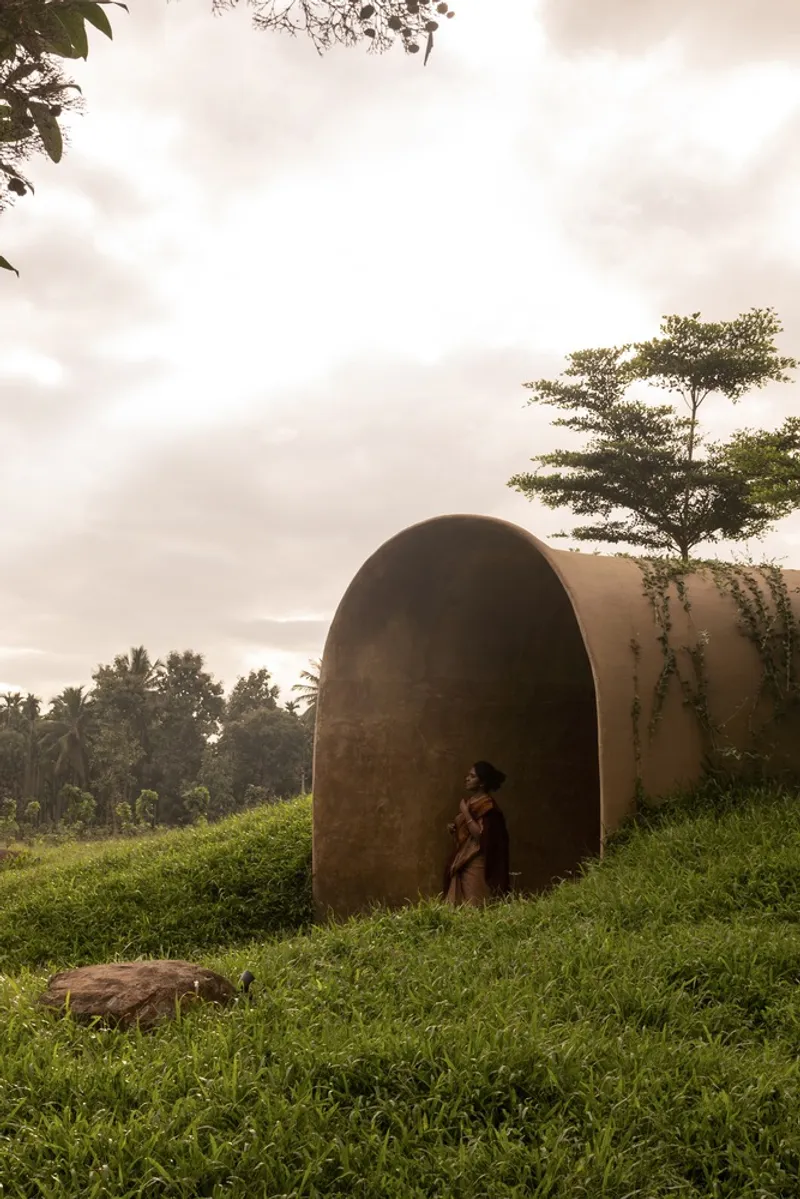 Entry tunnel: woman approaching the arched earth portal, grass slope, stepping stones, trees, hazy light