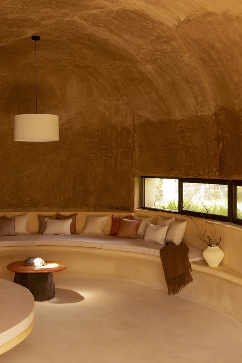 Sunken living: curved built-in sofa, cushions, vaulted earth ceiling, pendant lamp, strip windows, warm tones