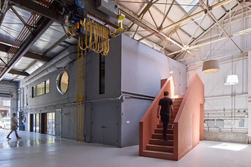 Salmon-colored steel stair with figure ascending beneath corrugated metal ceiling and hanging pendant lights
