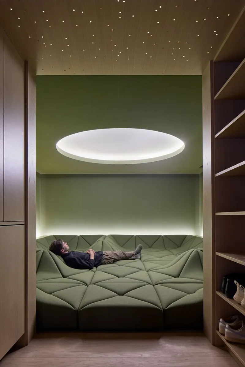 Recessed alcove with sage green quilted daybed beneath perforated ceiling and floating circular light fixture