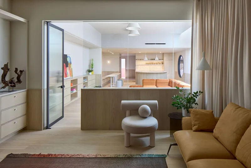 Living space with tan sofa looking through glazed partition toward kitchen and dining area