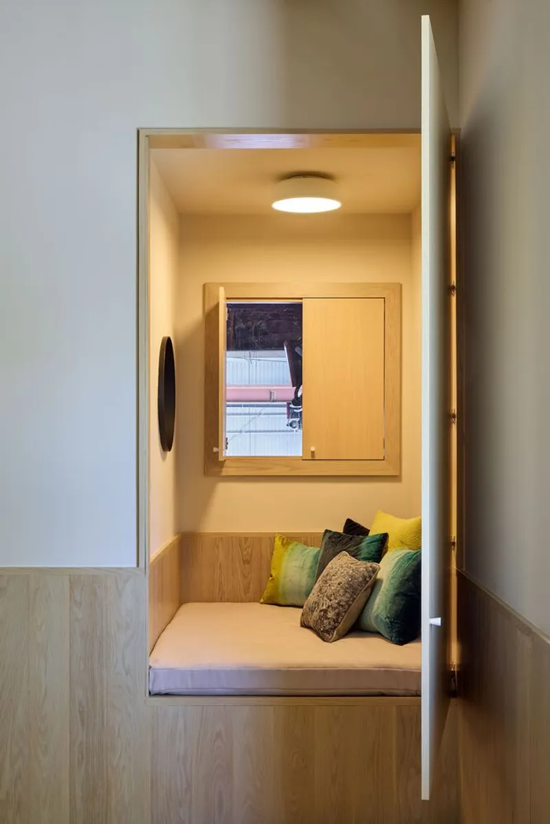 Light wood reading nook with built-in bench, cushions, and square window framing an exterior view