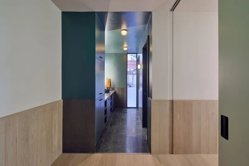 Corridor view through sliding door to galley kitchen with dark cabinetry and ceiling-mounted fixtures