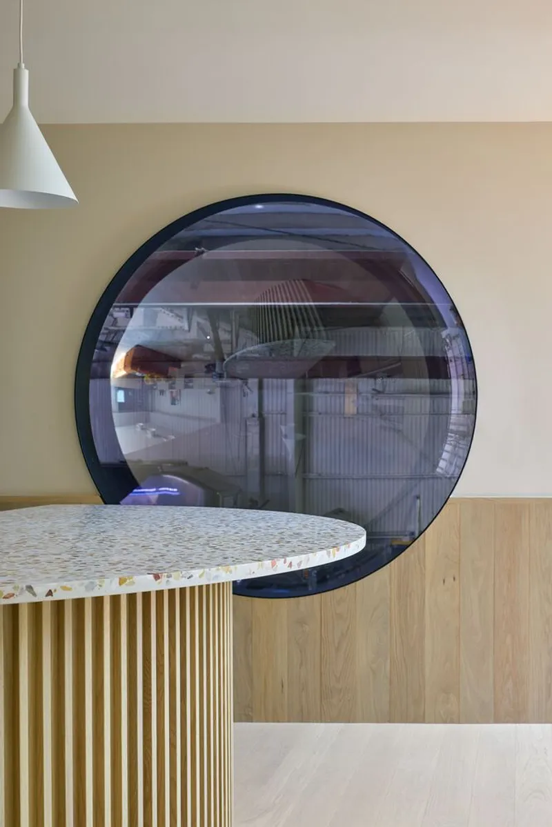 Dining area with terrazzo-topped fluted base and large circular window overlooking a courtyard