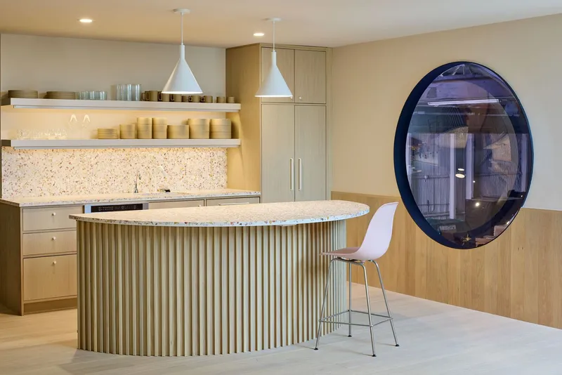Kitchen island with vertical fluted wood siding, terrazzo backsplash, and oval porthole window set in timber wall