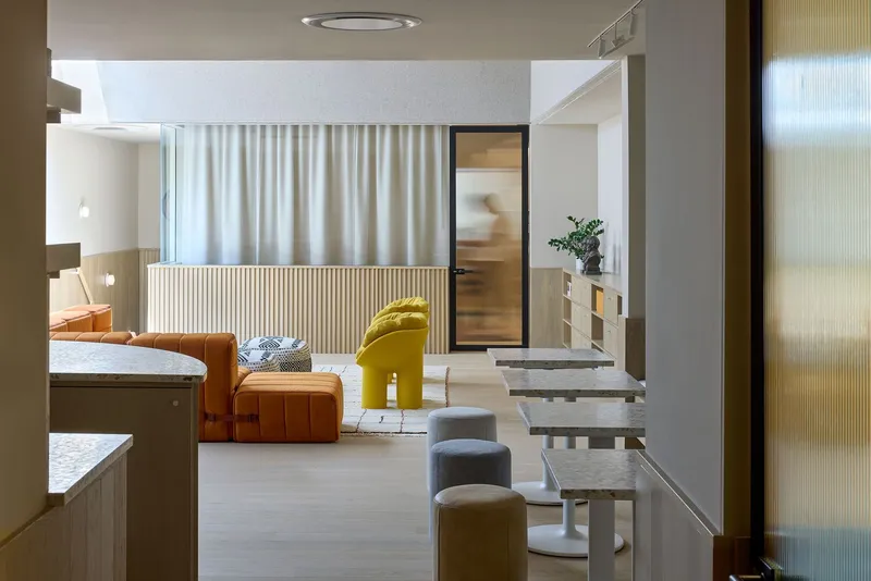 View through a translucent ribbed glass partition into a living area with fluted wood divider and cream curtains