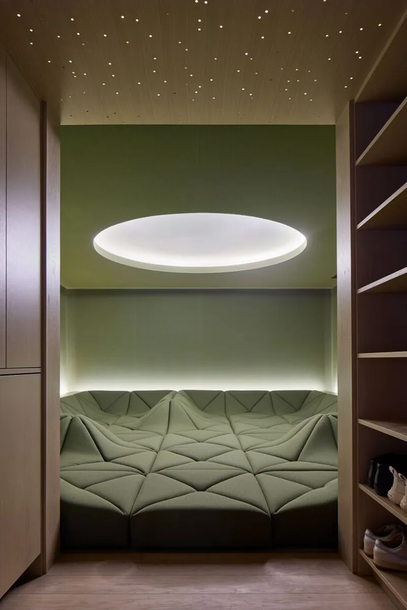 Sleeping nook with green fabric walls and a floating circular luminaire above quilted cushions