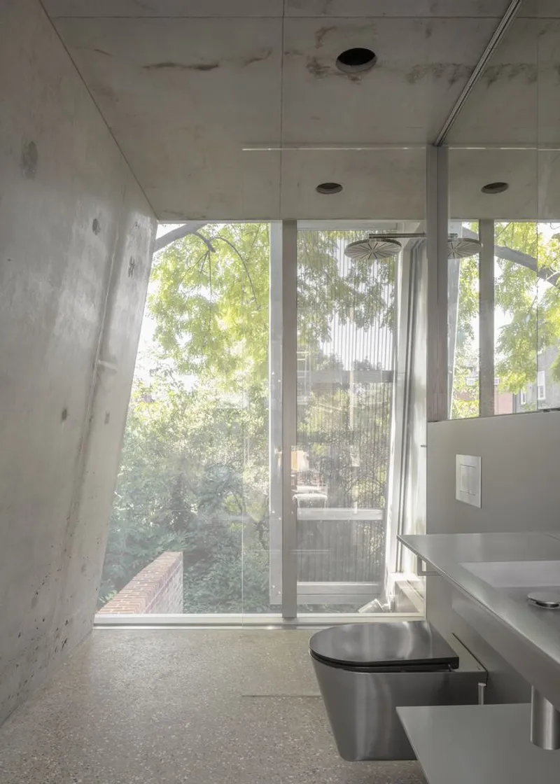 Bathroom with concrete walls, glass, and a view of tree canopy.