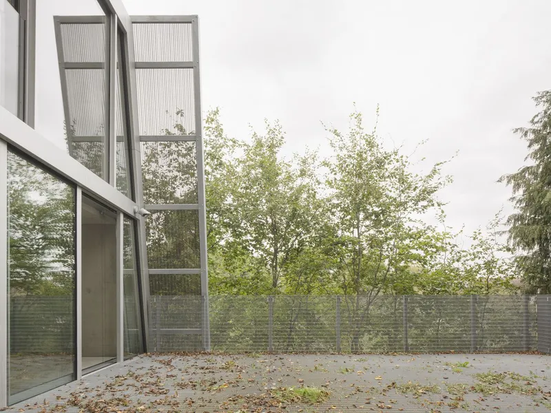 Terrace with angled glass facade and autumn leaves on the ground.