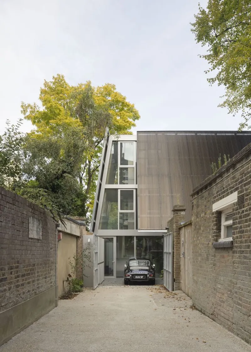 The mews approach: a narrow lane with the A-frame glass facade rising behind the boundary wall.