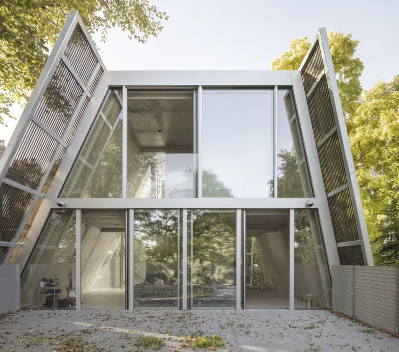 The A-frame glass facade with angled steel columns rises two storeys above the garden.