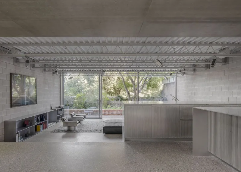 Ground floor open plan with concrete ceiling, exposed steel trusses, stainless steel island, and blockwork wall facing the mews.