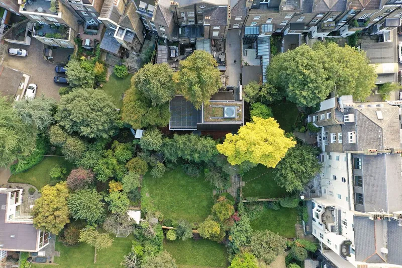 Aerial view directly above showing the house surrounded by mature garden trees and solar panels on the roof.