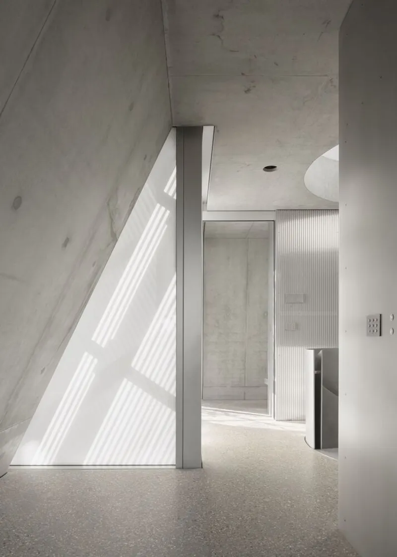 Interior corridor with angled concrete wall, light strips, and terrazzo flooring.