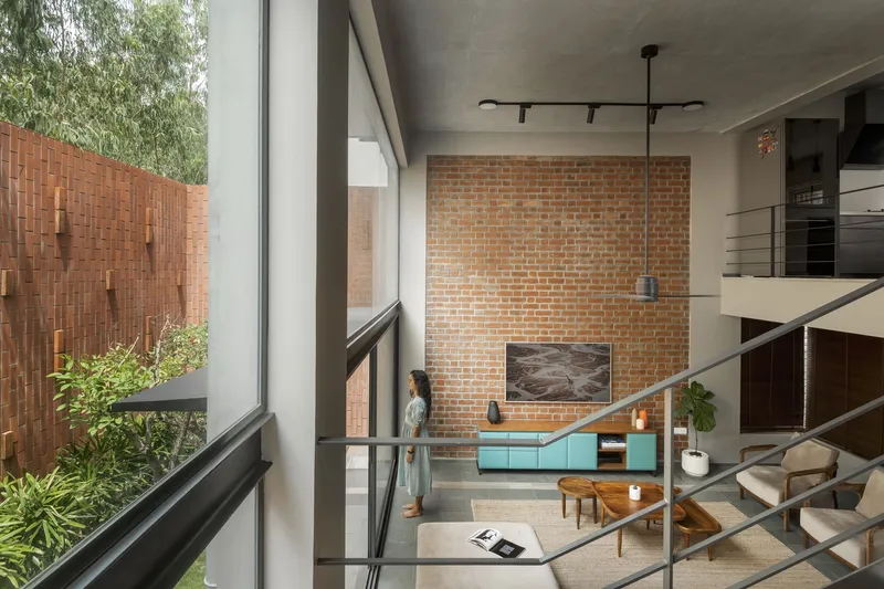 From the upper level: looking down to the living room, exposed brick TV wall, teal cabinet, sectional, jute rug, bamboo screen behind