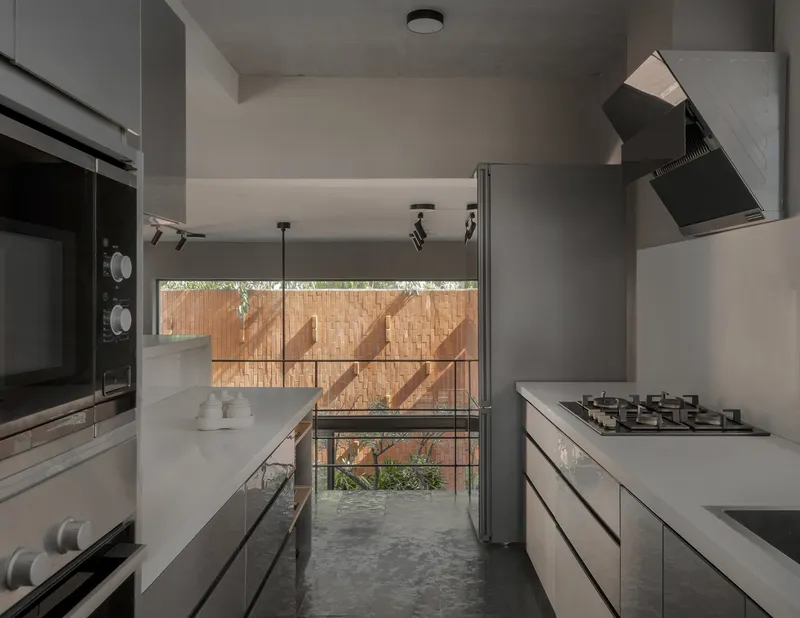 Kitchen: dark grey concrete walls and ceiling, light counter with gas hob, range hood, view through to the garden with brick screen