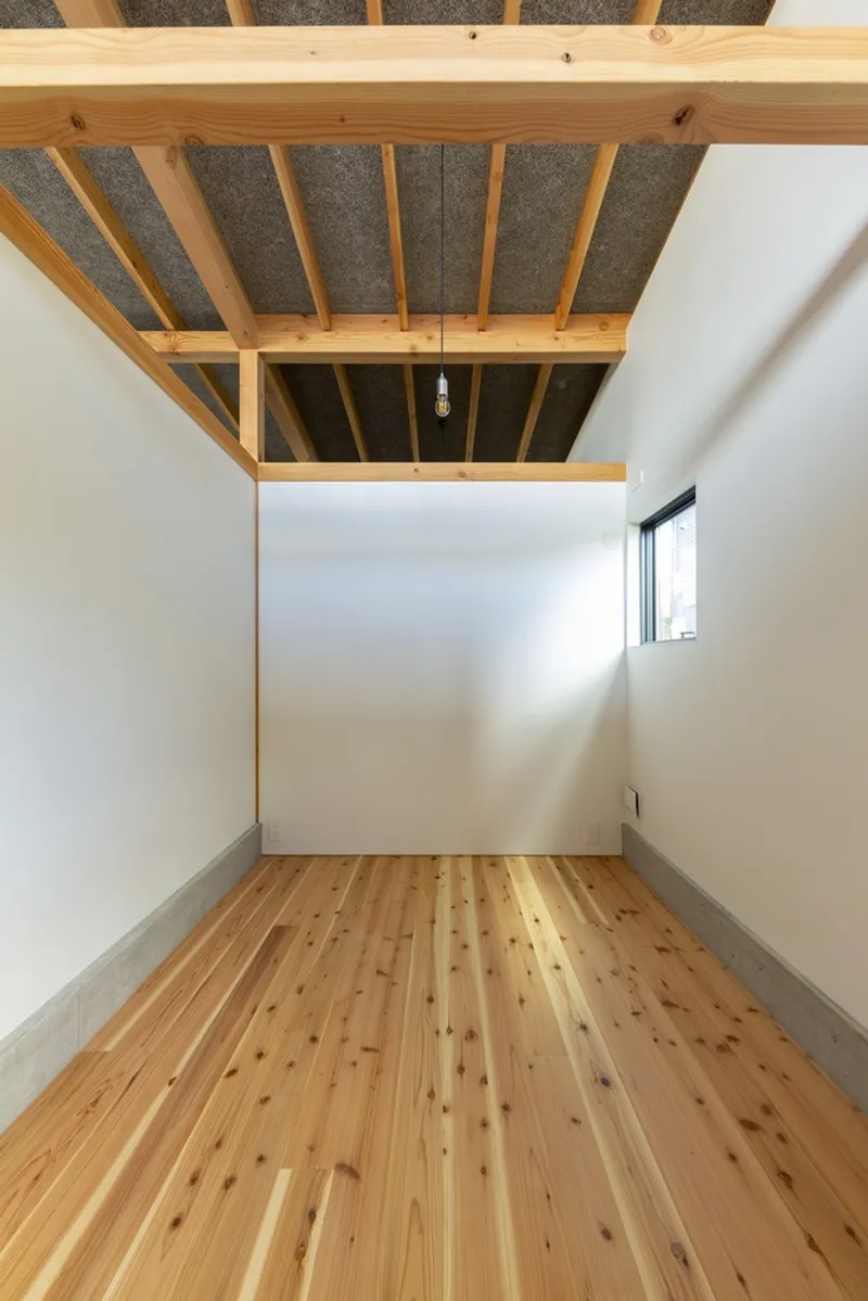 Bedroom: pale timber floor, white plaster walls, exposed timber rafter ceiling, small high window, minimal and unadorned
