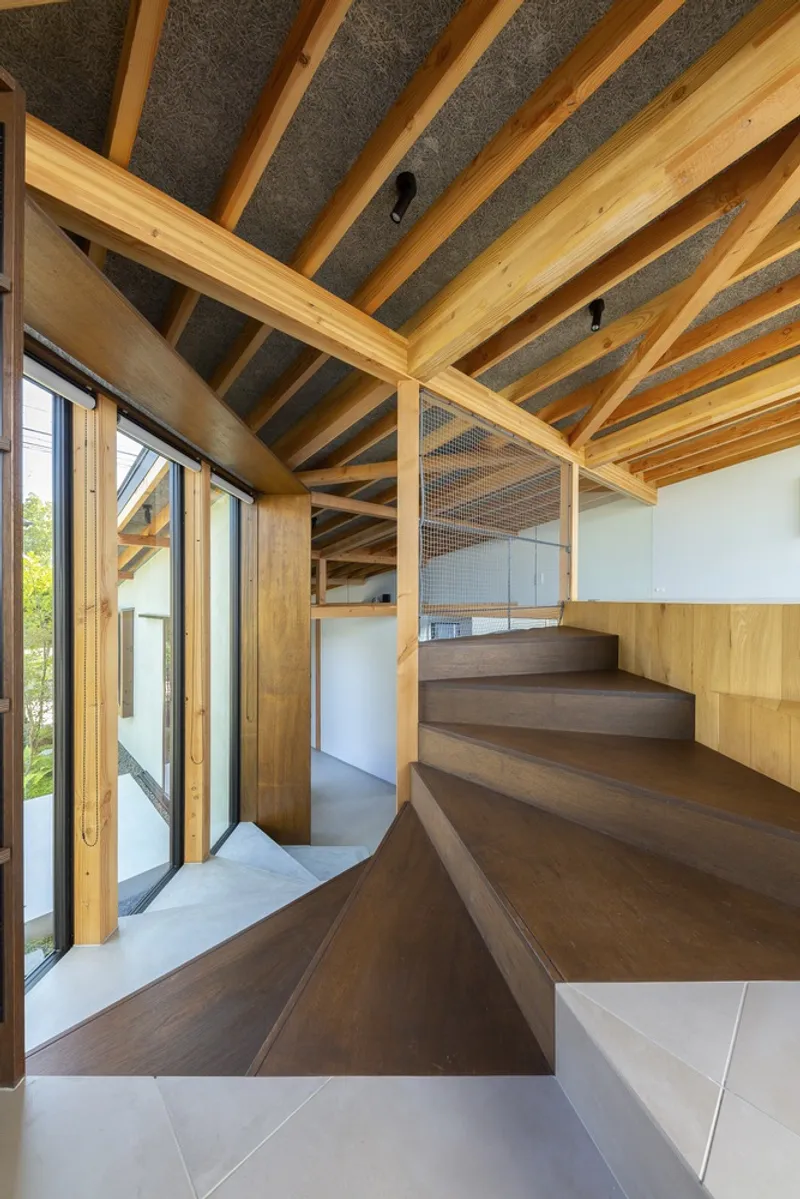 Stair void: angled timber stair with concrete wall at centre, exposed timber rafters, glass balustrade, concrete floor