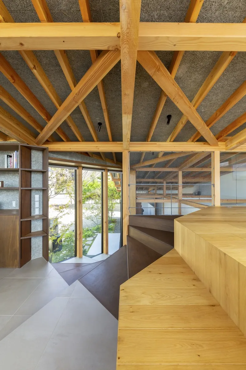 Double-height void: timber rafter ceiling and sloped roof, timber bench seat, glass wall to the garden with a tree visible, plaster walls