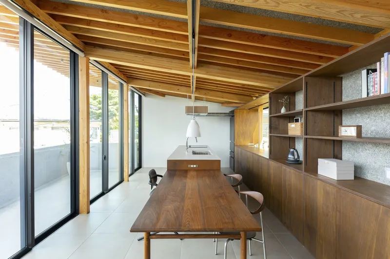 Dining and kitchen: timber dining table with metal stools, full-height dark timber storage wall, exposed rafter ceiling, south-facing glazing